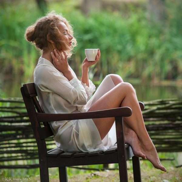 Женщина сидит с чашкой на стуле у плетня