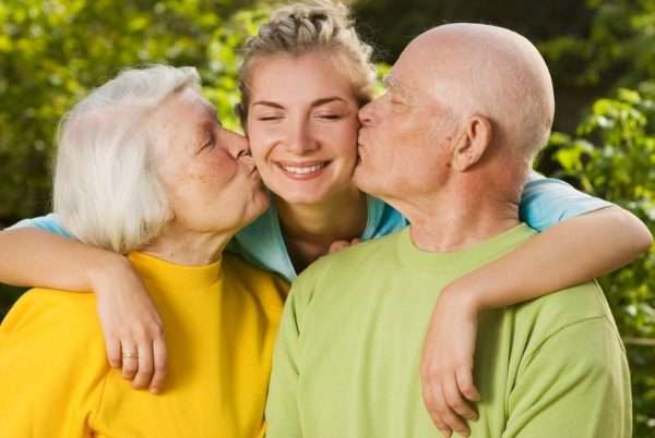 Пожилые люди целуют девушку в щёки