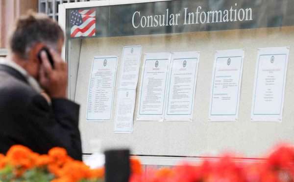 Мужчина с телефоном у доски объявлений с консульской информацией США